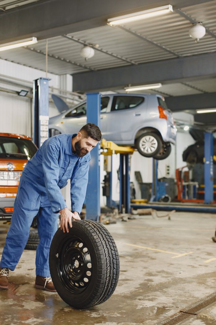 portfolio-03 Mechanic handling a tire in a busy automotive repair workshop.