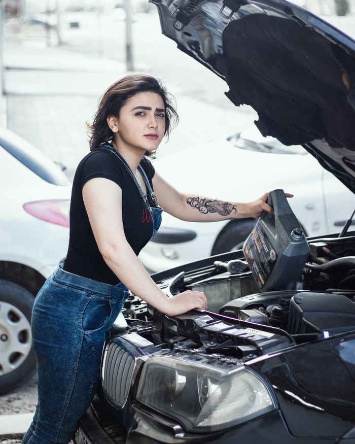 portfolio-01 Young female mechanic working on car engine outdoors in daylight.