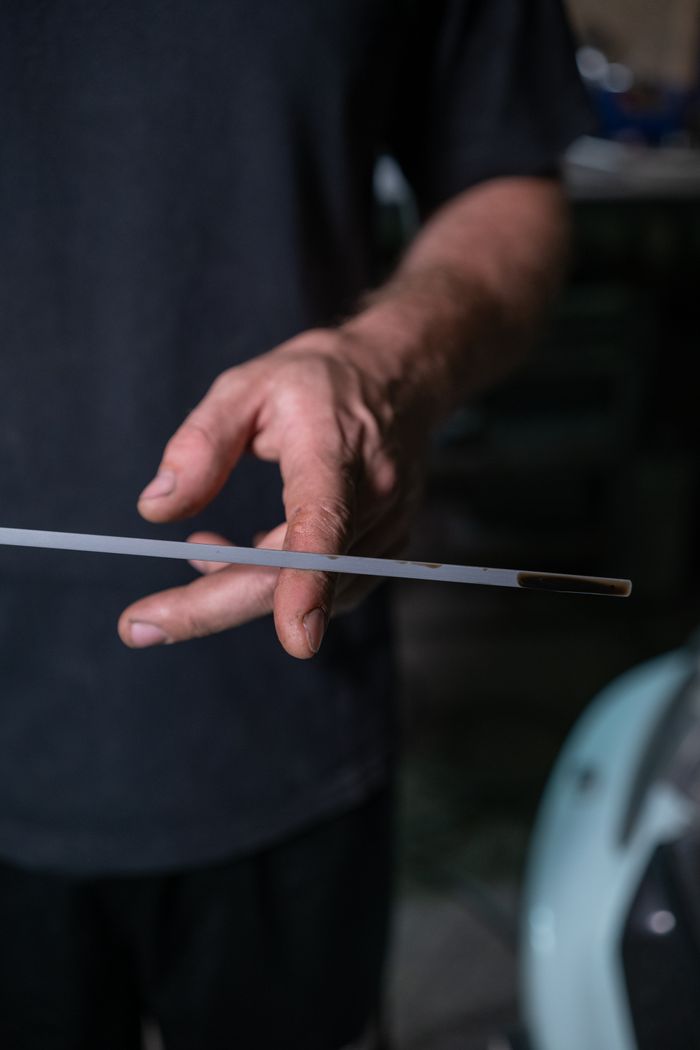 portfolio-05 Detailed close-up of a hand holding a dipstick to check engine oil level in a garage setting.