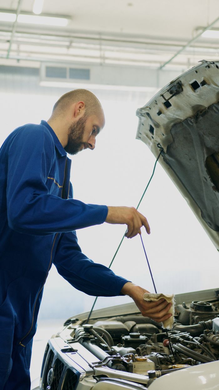 stats-img Mechanic inspecting car engine oil with dipstick in an automotive repair shop.