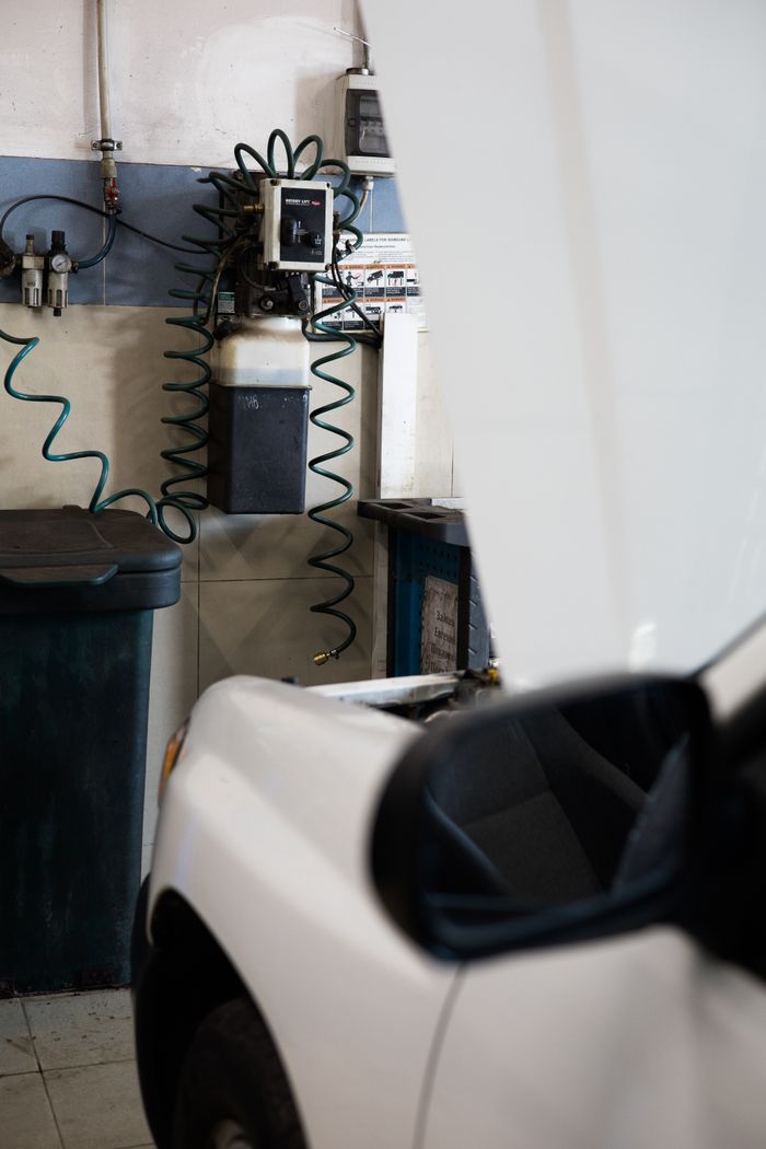 why-choose-us White car under maintenance in a well-equipped garage with tools and machines.