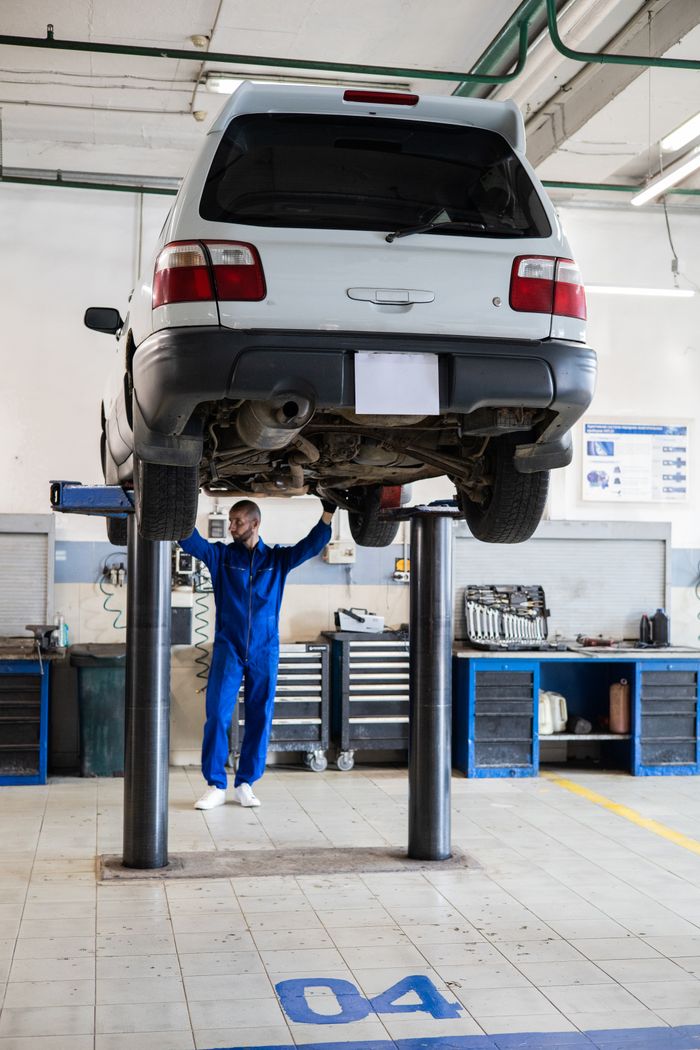 portfolio-06 Mechanic in blue coverall inspecting a lifted car in an auto repair shop.